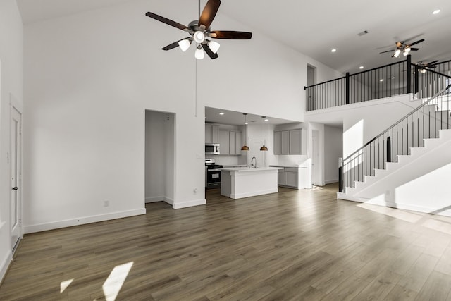 unfurnished living room featuring ceiling fan, sink, dark wood-type flooring, and a high ceiling