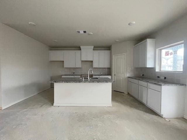 kitchen with decorative backsplash, white cabinetry, sink, and a kitchen island with sink