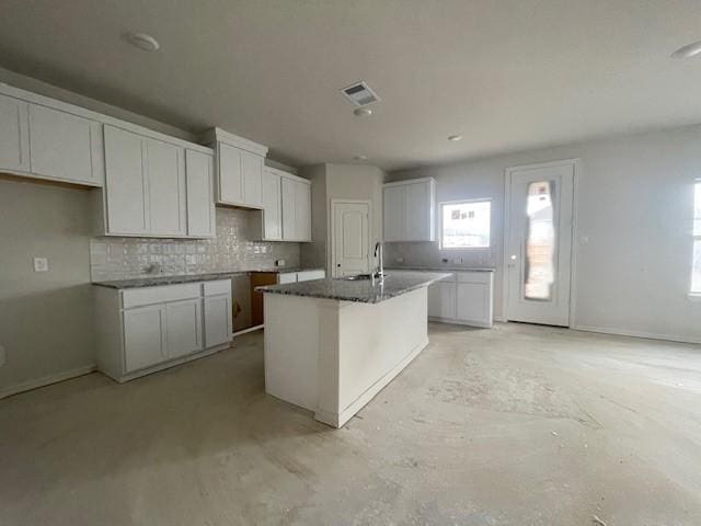 kitchen with dark stone counters, white cabinets, sink, an island with sink, and tasteful backsplash