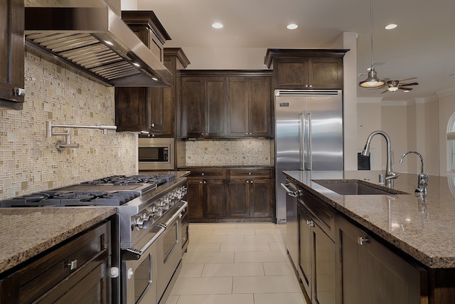 kitchen featuring decorative backsplash, wall chimney exhaust hood, light stone countertops, built in appliances, and sink