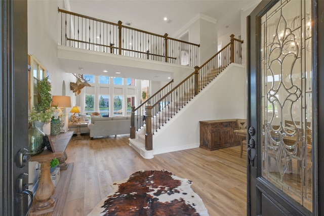 entryway with ornamental molding, light hardwood / wood-style flooring, and a high ceiling