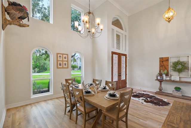 dining area featuring light wood-type flooring, crown molding, a high ceiling, and a chandelier