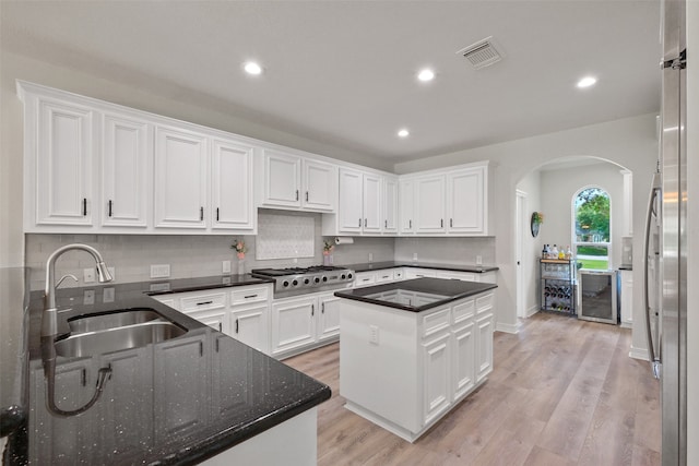 kitchen with sink, a kitchen island, white cabinetry, stainless steel appliances, and light hardwood / wood-style floors