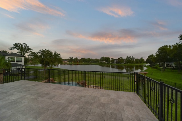 patio terrace at dusk with a water view and a yard