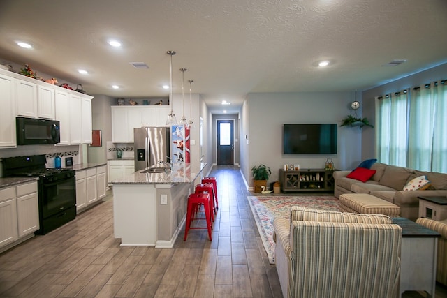 kitchen with light wood-type flooring, an island with sink, hanging light fixtures, a kitchen breakfast bar, and black appliances