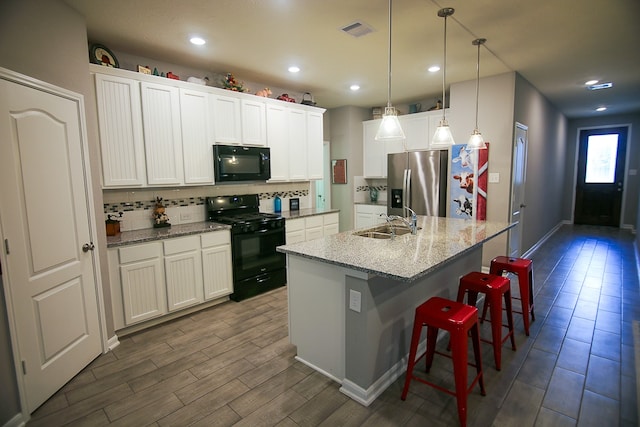 kitchen with white cabinets, sink, decorative light fixtures, a kitchen island with sink, and black appliances