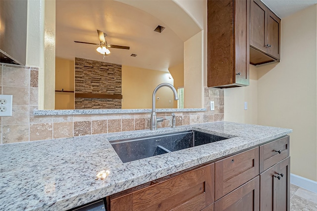 kitchen with sink, ceiling fan, light stone counters, and tasteful backsplash