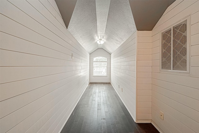 hallway with wood walls, a textured ceiling, and lofted ceiling