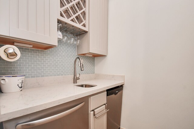 kitchen featuring tasteful backsplash, stainless steel dishwasher, sink, and light stone counters