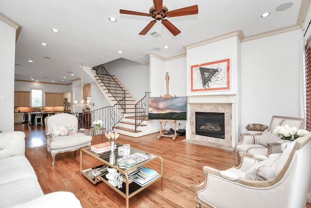 living room featuring ornamental molding, ceiling fan with notable chandelier, a tiled fireplace, and light wood-type flooring