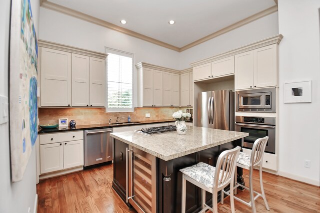 kitchen with appliances with stainless steel finishes, a kitchen island, beverage cooler, crown molding, and light hardwood / wood-style flooring