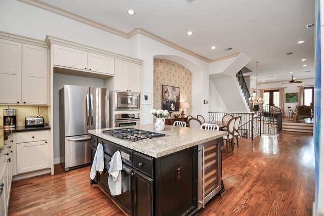 kitchen with wood-type flooring, ornamental molding, beverage cooler, appliances with stainless steel finishes, and ceiling fan