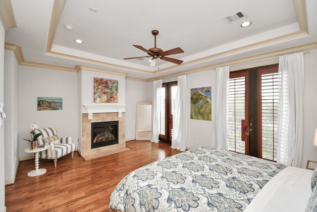 bedroom with multiple windows, hardwood / wood-style floors, ceiling fan, and a raised ceiling