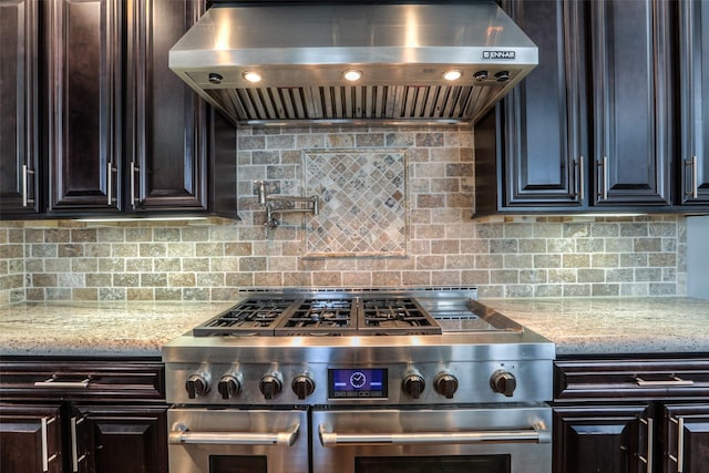 kitchen featuring stainless steel range, backsplash, light stone countertops, and wall chimney range hood