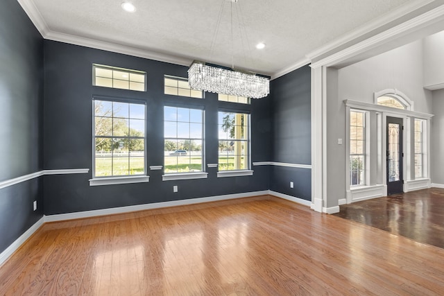 spare room with wood-type flooring, a textured ceiling, crown molding, and a notable chandelier