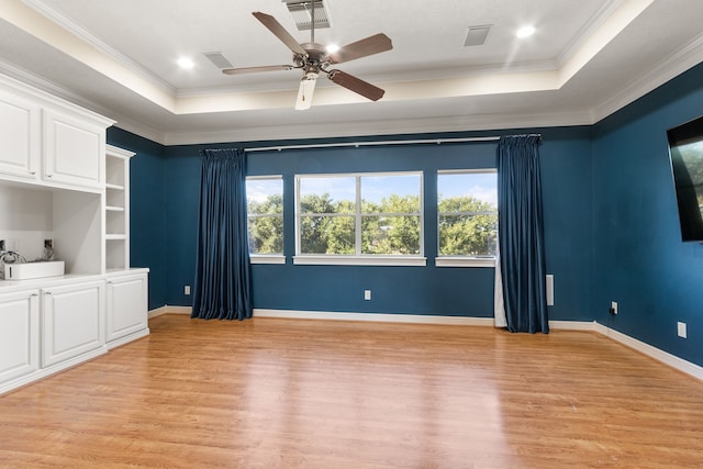 spare room featuring light hardwood / wood-style floors, a tray ceiling, crown molding, and ceiling fan