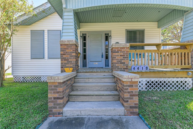 view of exterior entry with a porch and a yard