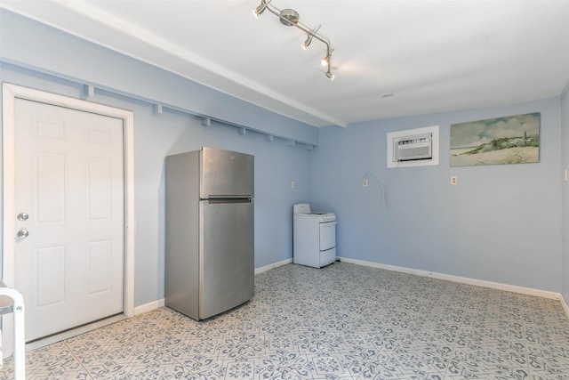 basement with freestanding refrigerator, baseboards, a wall unit AC, and washer / clothes dryer