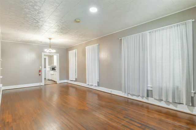 spare room with baseboards, crown molding, a chandelier, and wood finished floors