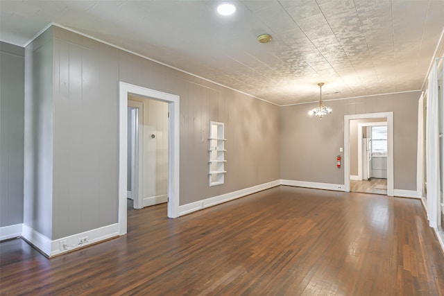 unfurnished room with ornamental molding, an inviting chandelier, and dark wood-type flooring