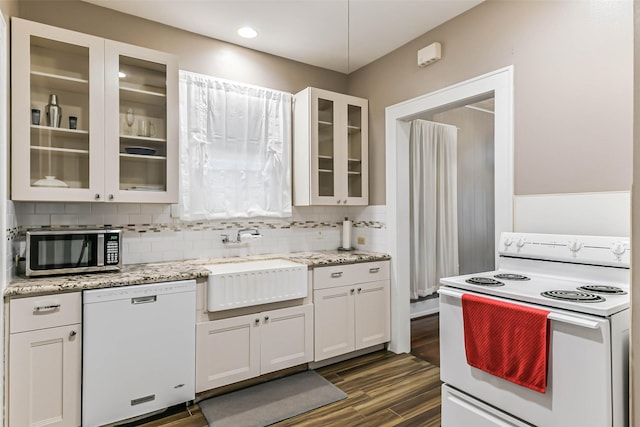 kitchen featuring light stone counters, backsplash, a sink, white appliances, and glass insert cabinets