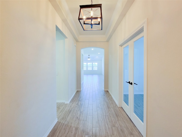 hallway with a raised ceiling, light hardwood / wood-style floors, an inviting chandelier, and french doors