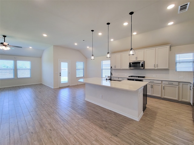 kitchen featuring appliances with stainless steel finishes, vaulted ceiling, ceiling fan, a kitchen island with sink, and sink