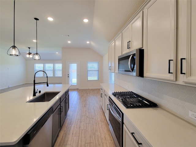 kitchen featuring hanging light fixtures, sink, appliances with stainless steel finishes, light wood-type flooring, and vaulted ceiling