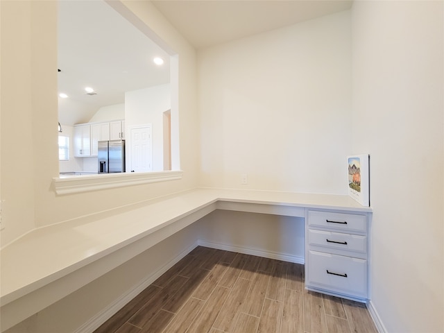 unfurnished office featuring light wood-type flooring, built in desk, and lofted ceiling