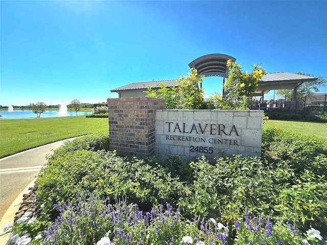 community sign with a water view and a yard