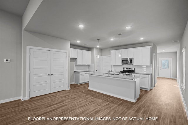 kitchen with appliances with stainless steel finishes, decorative light fixtures, white cabinetry, an island with sink, and backsplash