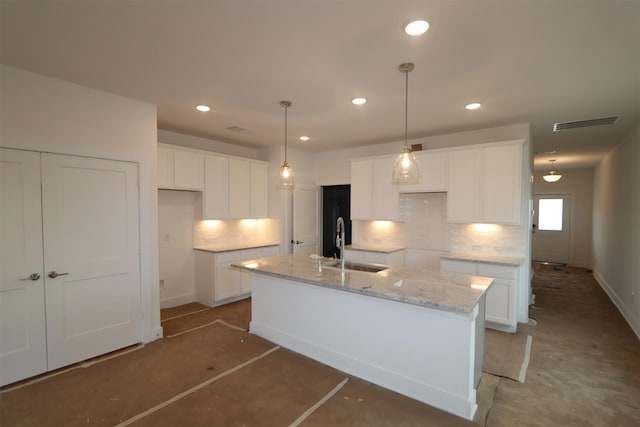 kitchen featuring light stone countertops, hanging light fixtures, white cabinets, and a kitchen island with sink