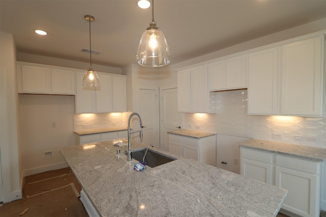 kitchen featuring an island with sink, decorative light fixtures, sink, and white cabinets