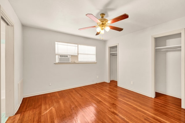 unfurnished bedroom featuring cooling unit, two closets, light hardwood / wood-style floors, and ceiling fan