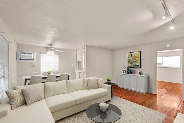 living room featuring rail lighting, wood-type flooring, a wall mounted air conditioner, and plenty of natural light