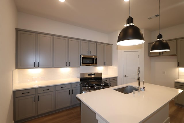 kitchen with decorative light fixtures, stainless steel appliances, a center island with sink, backsplash, and sink