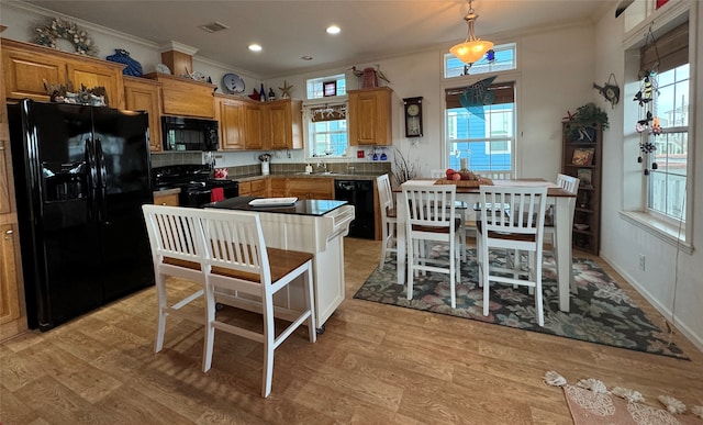 kitchen with light hardwood / wood-style flooring, black appliances, hanging light fixtures, and a kitchen island