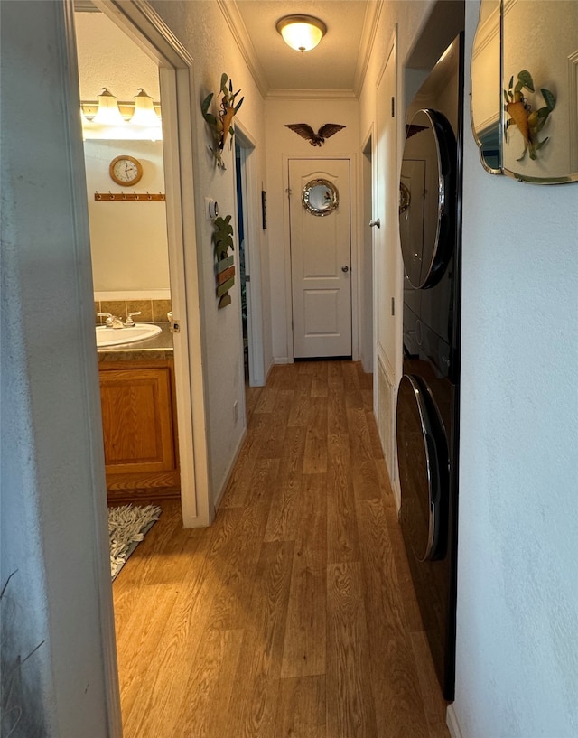 hallway with ornamental molding, sink, hardwood / wood-style floors, and stacked washing maching and dryer