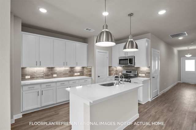 kitchen with white cabinetry, appliances with stainless steel finishes, a kitchen island with sink, pendant lighting, and sink