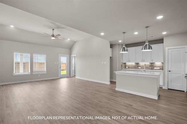 kitchen featuring lofted ceiling, backsplash, a center island with sink, white cabinetry, and hanging light fixtures