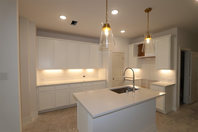 kitchen featuring decorative light fixtures, tasteful backsplash, a center island with sink, sink, and white cabinetry