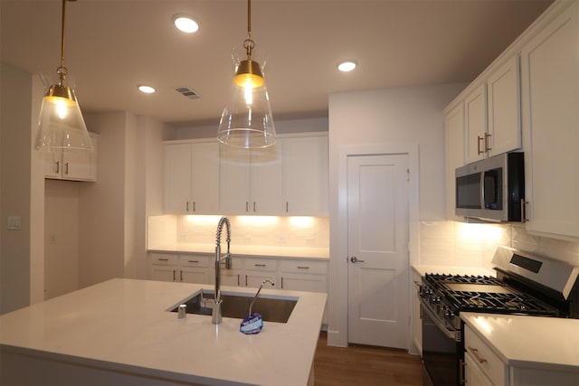 kitchen featuring an island with sink, stainless steel appliances, decorative light fixtures, and sink