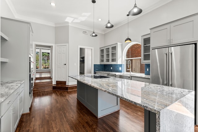 kitchen with high end refrigerator, light stone countertops, a center island, and pendant lighting