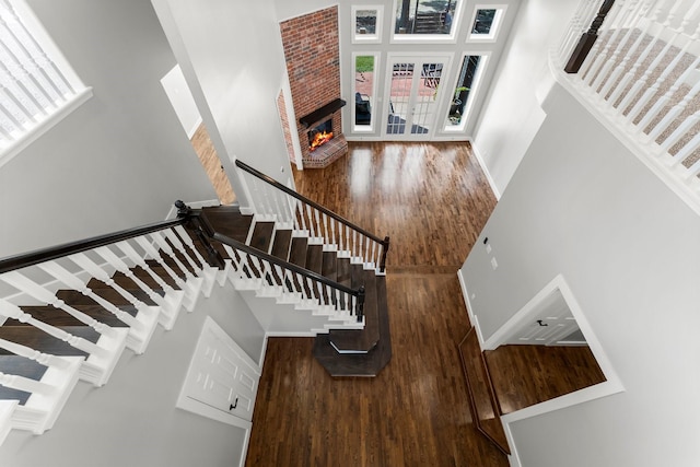 stairs featuring hardwood / wood-style floors, a towering ceiling, and a brick fireplace