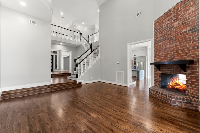 unfurnished living room featuring hardwood / wood-style flooring, ornamental molding, a high ceiling, and a brick fireplace