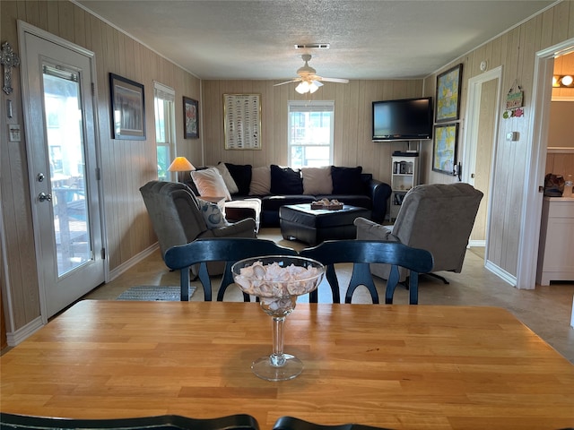 living room with ceiling fan, a textured ceiling, and wooden walls