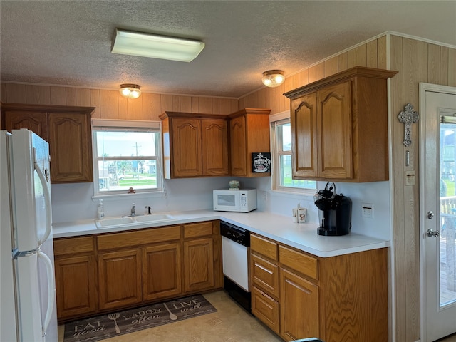 kitchen featuring a textured ceiling, white appliances, wooden walls, and sink