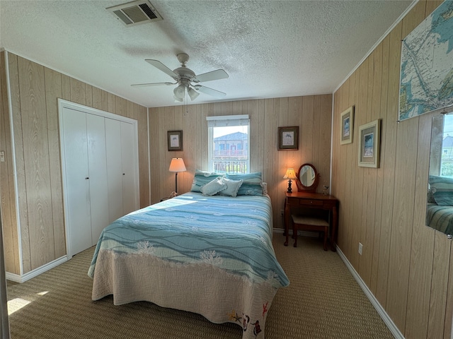 bedroom with wood walls, a closet, a textured ceiling, ceiling fan, and light colored carpet