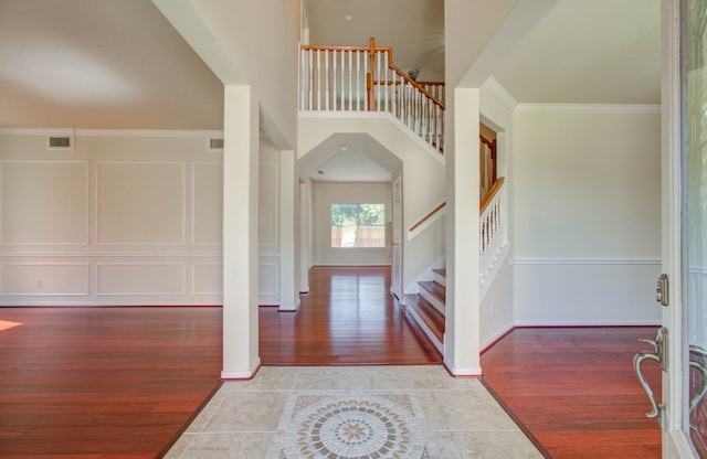 foyer featuring wood-type flooring, crown molding, and a high ceiling