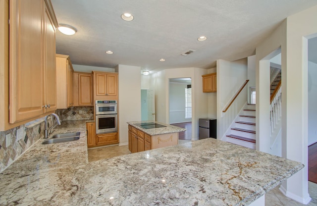 kitchen featuring light stone counters, tasteful backsplash, sink, a kitchen island, and double oven